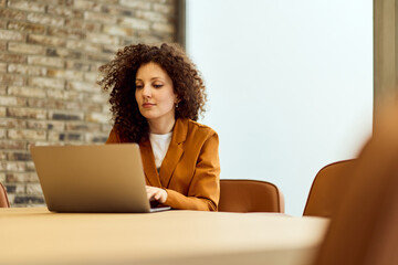 Professional Woman Working on Laptop In A Modern Office With Brick Wall Accent And Natural Light