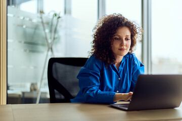 Professional Woman in Blue Shirt Working on Laptop in Bright Modern Office Space Today
