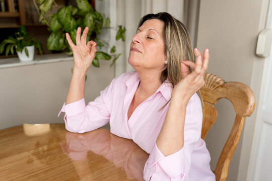 Mature woman meditating with eyes closed, finding peace and relaxation, practicing mindfulness for stress relief at home