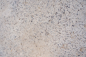 Textured concrete surface with embedded aggregate and subtle swirl pattern. Construction material, flooring, industrial background. Real photo