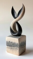 A studio shot of an abstract wooden sculpture. The sculpture is composed of two intertwined, leaf-like shapes in black and white, mounted on a cube-shaped base.