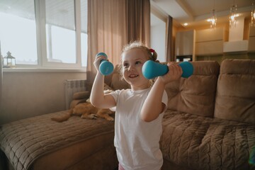 A joyful 4-year-old girl does morning exercises in a bright living room. Authentic moment of child...