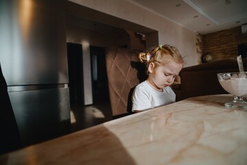 A cheerful 4-year-old girl prepares for breakfast in a bright morning living room. Authentic childhood moment of family routine and natural morning energy