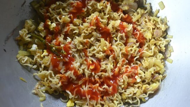 Noodles are being prepared by boiling instant noodles and mixing them with scrambled eggs, saut&eacute;ed vegetables, sauces, and Indian spices. Noodles were kept on a plate. Vegetable Masala Noodles