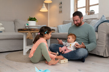 Father playing with his two daughters, a 5 year old girl and a 5 months baby girl, in their living room.