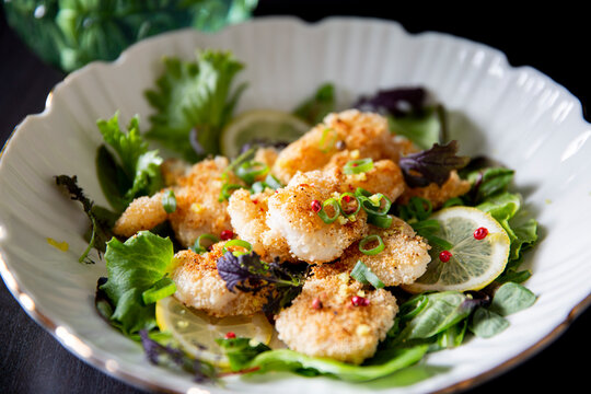 Crispy panko cod cheeks served on fresh gourmet greens with lemon and pink peppercorns - a premium seafood dish for fine dining menus and culinary