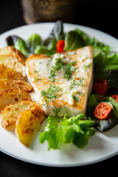 Delicious fried swordfish steak with roasted potato wedges, fresh greens, and creamy sauce. Healthy seafood dinner meal concept.