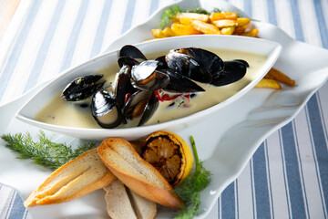 Gourmet mussels in white wine cream sauce with french fries, toasted baguette, lemon, and dill. Elegant seafood meal