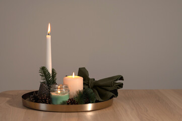 Beautiful cozy candlelight backdrop with empty copy space, aesthetic Christmas still life with lit candles and fir tree branches on tray on neutral beige wooden table background