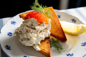 Classic Swedish Toast Skagen appetizer on white plate: shrimp salad, red caviar, dill garnish, lemon wedge, and crispy butter toast.