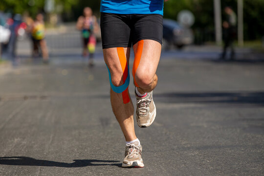Runner feet in kinesiotape running marathon on road