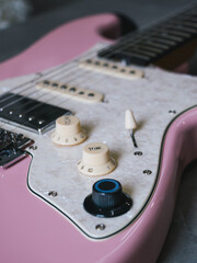 Close-up of a pink electric guitar with pearl pickguard and cream knobs. This image showcases the details of an electric guitar, highlighting its unique color and design elements