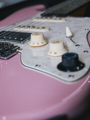Close-up of a pink electric guitar with white pickguard and knobs. This image showcases the details of an electric guitar, highlighting its color and components