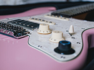 Close-up of a pink electric guitar with white pickguard and cream knobs. This image showcases the details of a pink electric guitar, highlighting its design and components