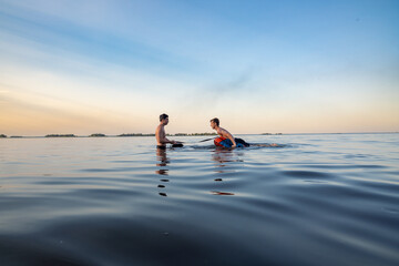 Two men engage in water sports training on a calm lake at sunset or sunrise, showcasing teamwork and outdoor activity. Ideal for themes of fitness, recreation, and natural beauty.