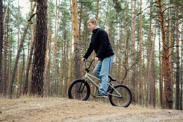 Fototapeta premium Young person on a BMX bike riding through a serene pine forest, capturing the spirit of outdoor adventure and youthful energy. Ideal for themes of nature, sport, and active lifestyle.