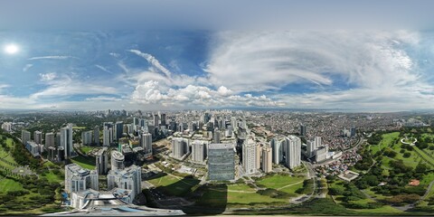 High altitude 360 aerial view over Bonifacio Global City business district in Taguig with Manila American Cemetery and green parks under dramatic clouds in Metro Manila, Philippines.