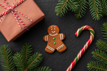 Christmas Celebration Flat Lay with Gingerbread Man, Candy Cane, Gift Box, and Fir Branches on Black Background