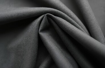 Obraz premium Closeup view of dark grey jersey fabric with soft texture, subtle ribbed pattern. Material drapes, folds, creating shadows, highlights. Versatile textile displays fine threads, smooth surface.
