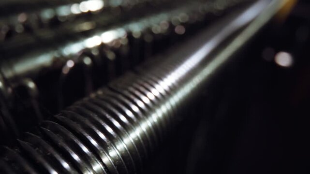 Close macro shot shows polished metal rods catching soft highlights while thin textile threads run between them, creating a moody industrial atmosphere with shallow focus
