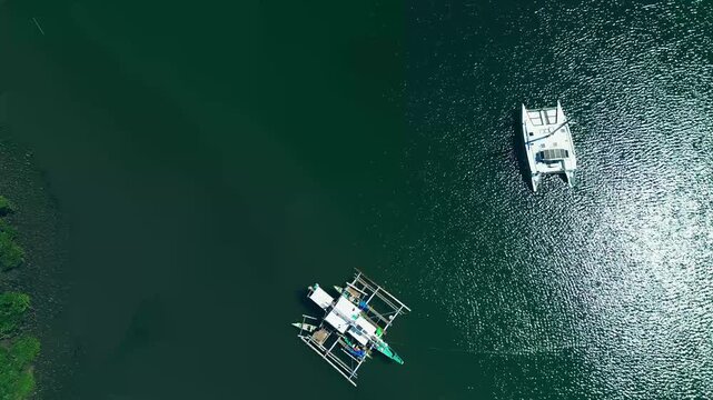 Drone view of tilt down to a catamaran and outrigger fishing boat floating on serene glittering waters of Tambobo Bay in Siaton, Negros Oriental, Philippines