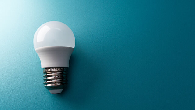 a white plastic LED bulb isolated on a smooth, solid blue-green surface. The large copy space is perfect for advertising or health campaigns.