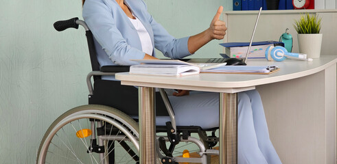 Businesswoman wheelchair giving thumbs up while working on laptop at modern office desk concept