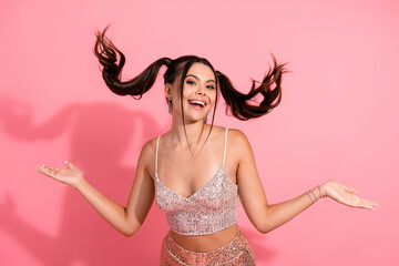 Joyful young brunette woman in glittery pink top and sequin skirt dances with playful ponytails...