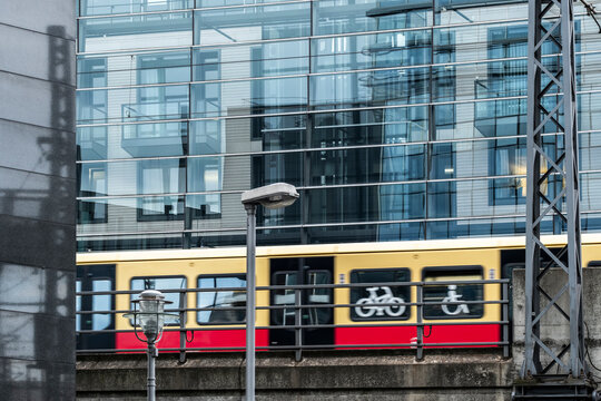 Berlin mobility scene with a yellow train passing a glass facade, showing reflection, contrast, movement and strong urban transit structure