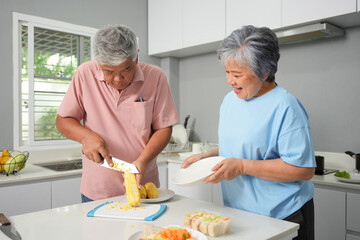 Senior Couple Preparing Fresh Corn Together In The Kitchen, Elderly Man Cutting Corn While His Wife Assists With A Smile, Happy Older Couple Cooking And Preparing Ingredients At Home