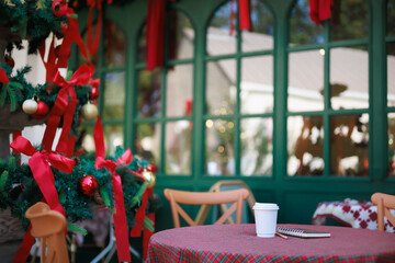 close-up view, white coffee cup with notebook on red patterned tablecloth with christmas tree and item decorate, celebrate in christmas holiday