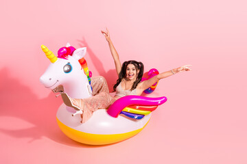 Young woman rides a colorful inflatable unicorn float in a pink studio smiling and posing for a...