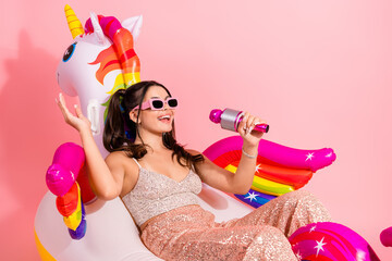 Glamorous young woman in pink party outfit with unicorn inflatable singing into a shiny microphone...