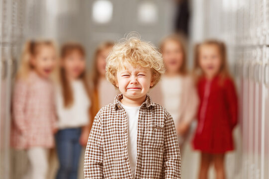 Crying boy in school hallway feels bullied by laughing peers around him