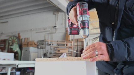 The carpenter is tightening screws in a piece of furniture with a cordless drill. Furniture assembly, carpentry, and a do-it-yourself (DIY) project.