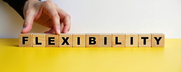 Man hand arranges wooden cubes spelling FLEXIBILITY. This concept photo represents business adaptability and change. A bright yellow surface and white background create a clean, modern look.