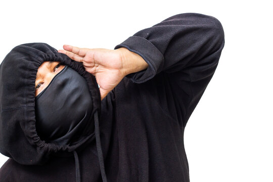 Unidentifiable person in black hoodie and balaclava makes a protective gesture with their hand, symbolizing anonymity, secrecy, and the concept of hidden identity