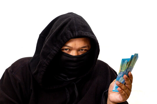 A mysterious figure in a dark hoodie with their face obscured, holding a wad of banknotes, symbolizing illicit money, a hidden identity, or questionable financial dealings