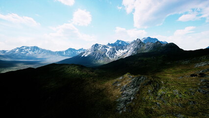 Fototapeta premium A stunning view of rugged mountain peaks adorned with snow reaches towards a bright blue sky. Lush green valleys cascade beneath, inviting adventure and exploration in natures beauty.
