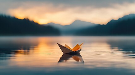 A small folded paper boat floats gently on a calm lake at sunrise with misty mountains in the background and soft orange light illuminating the water creating a serene and peaceful atmosphere