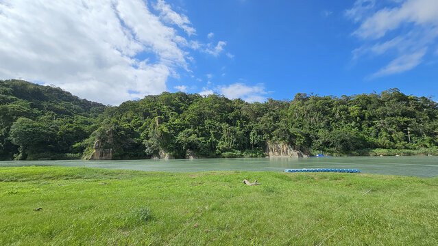 Taipei City, Taiwan. November 15, 2025. Scenic riverside green grass path in Xindian Bitan with open mountains trees landscape and clear sky creating a relaxing eco-friendly outdoor atmosphere - Powered by Adobe