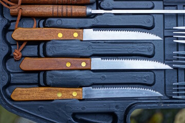 a row of three old knives with brown handles lie in a black box