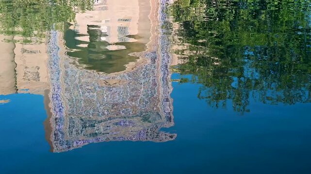 A rippling reflection of the Nadir Divan Begi Khanaka in the pond at Lyabi Hauz Square in Bukhara, Uzbekistan. The water surface captures the colors and patterns of the historic facade, creating a sof