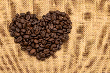 Roasted coffee beans in a heart shape on a sack of coffee background , with copy space , top view