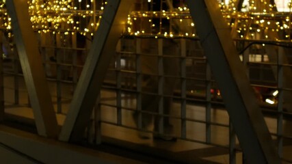 Person Walking Through Illuminated Bridge Passage: Motion Blur Figure on Modern Walkway with Golden String Lights Night Scene - Powered by Adobe