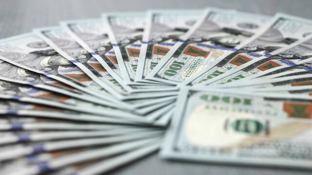 Fanned out stack of hundred dollar bills on a wooden surface, showcasing intricate designs and vibrant colors, representing wealth and financial prosperity in a modern context