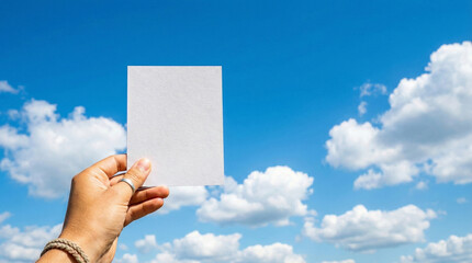  A hand holding a flyer up against a blue sky with fluffy white clouds, summer vibe