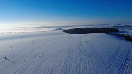 sunny day, snowy field, winter landscape, Czech countryside, aerial drone view, bright sky, fresh snow, open farmland, peaceful atmosphere, winter scenery