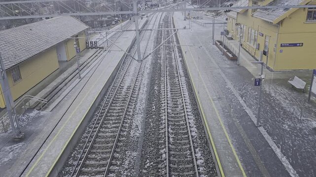 Camera tilts up over snow covered tracks showing Dale station and mountains in icy winter valley