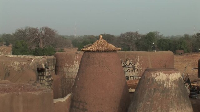 Traditional earthen granaries with conical thatched roofs in a rural landscape of northern Ghana near the Burkina Faso border.